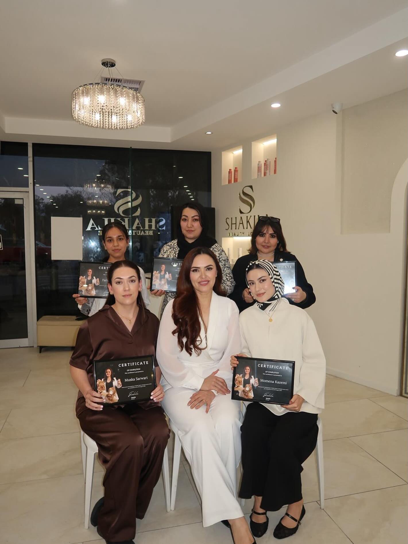 Shakila seated with her graduating students, each holding a certificate